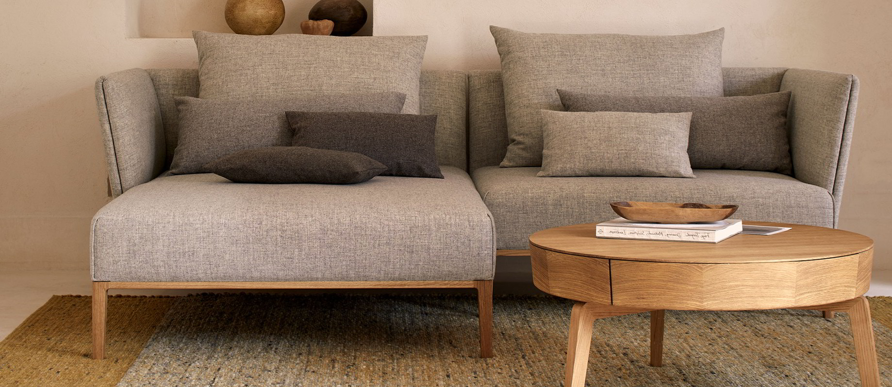 Graues Sofa steht auf einem grauen Teppich, ein Holzcouchtisch steht davor